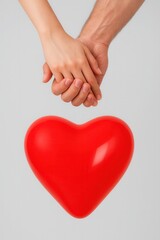 Two hands clasp each other, holding a shiny red heart, symbolizing love and connection against a neutral background