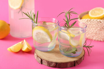 Glasses and bottle of fresh lemonade with rosemary on pink background
