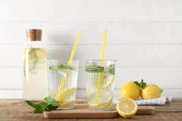 Glasses and bottle of fresh lemonade with mint on wooden table