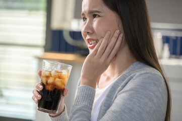Young Asian woman touching her cheek and mouth feeling pain from toothache, decay or sensitivity...
