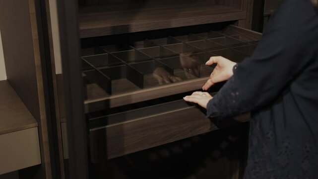 A woman's hand opens an empty wardrobe and reveals drawers for storing things. Modern storage furniture with neatly organized and efficient drawers for use