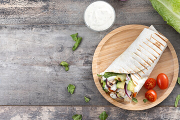 A delicious grilled chicken wrap with vegetables and avocado on wooden table. Top view. Copy space