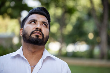 Thoughtful and pensive South Asian young adult man looking up, aiming at life goal mood or expression