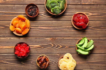 Frame made of bowls with different candied fruits on wooden background