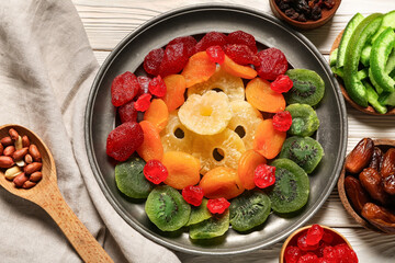 Plate and bowls with different candied fruits on white wooden background