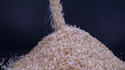 Brown cane sugar pouring into pile on black background. Excessive sugar content in various products. Nutrition. The benefits or the danger of sugar consumption to health concept. Slow motion - Powered by Adobe
