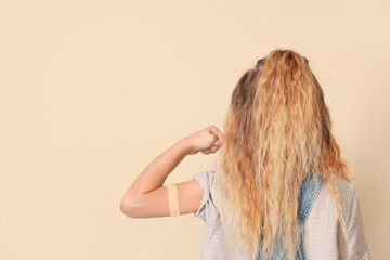 Little girl with applied patch after vaccination showing muscles on beige background, back view