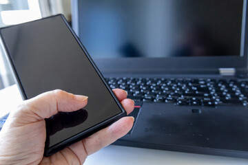 Senior hand holding smartphone near laptop 