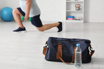 Sports bag with water bottle against senior man training at gym, closeup