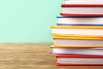 Stack of colorful books on wooden table against turquoise background