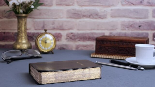 Bible falling for study on gray table with glasses and clock in the morning. Preparation for communion and worship concept. Slow motion