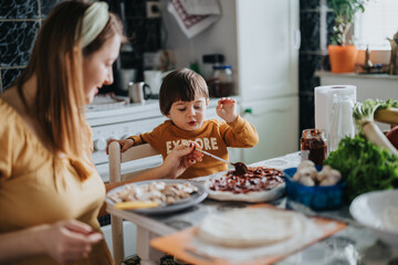 Mother and young child preparing homemade pizza in a cozy kitchen, working together with fresh ingredients and bonding during a joyful cooking activity.
