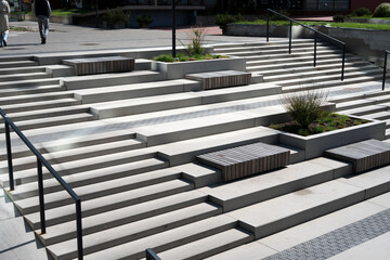sunlit urban plaza staircase composed of staggered concrete terraces, integrated wooden benches,...
