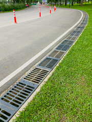 Curved road with orange traffic cones and drainage system runs alongside grassy area