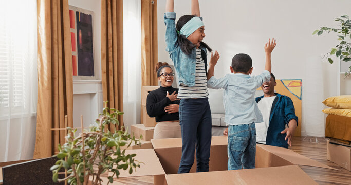 After the move, a family plays among unpacked boxes. The parents find their kids hiding inside one, and everyone laughs, enjoying the first moments in the new home.