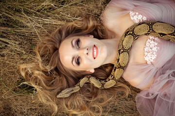 girl in a fluffy dress with a boa constrictor snake in nature