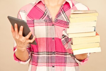 Close-up of a woman in a checked shirt holding and e-reader in one hand and a stack of books in the other