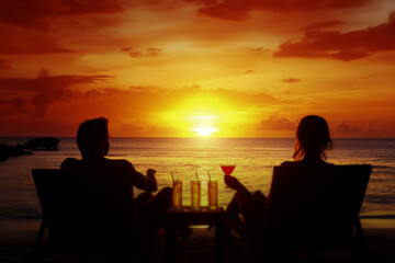 Obraz premium Two people lying on sun loungers and drinking cocktails at a sunset beach