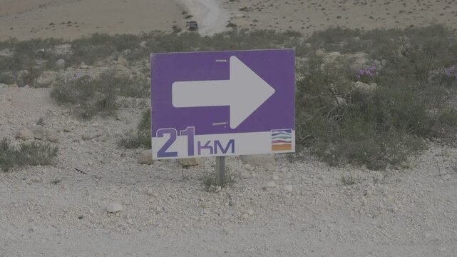 Directional race sign on dirt path shows runners where to turn during endurance event, 21km