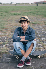 Teenager girl wearing hat sitting on skateboard relaxing in outdoor area