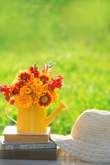 bright flowers bouquet in yellow watering can and books on table in garden, natural background. romantic atmosphere nature image. relax time. composition with flowers. summer season.