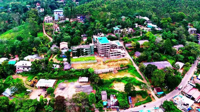 A residential complex under construction emerges from forested terrain near a Sri Lankan town, surrounded by winding roads, tropical trees, and scattered village homes.
