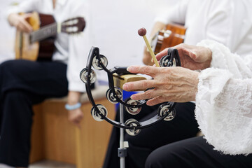 Close-up of an elderly woman’s hands playing a tambourine at a folk concert, capturing rhythmic...