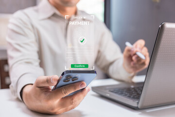 A person uses a smartphone to make a secure online payment with biometric authentication near a laptop.