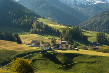 Visit Italy. Santa Maddalena wakes in soft golden light, church spire rising beneath the jagged...