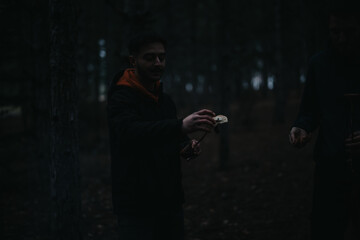 A person seen outdoors in a forest participates in cooking together, emphasizing friendship and outdoor activities in a natural setting under subdued lighting conditions.