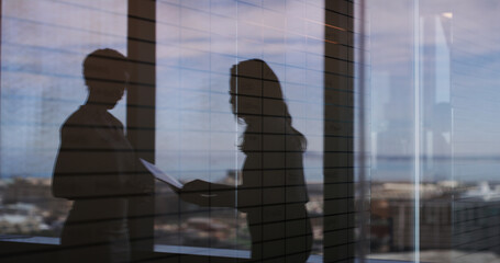 Discussion, shadow and business women in office by window with documents for finance report. Meeting, paperwork and silhouette of female financial advisors with company budget planning in workplace.