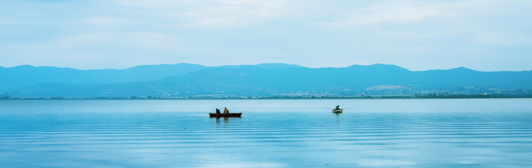Serene minimalist seascape featuring lone fishing boat floating on mirror-like calm waters with...