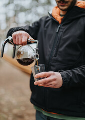 A person enjoying a warm drink outdoors during a winter picnic, focusing on hands pouring the beverage. Nature and leisure exemplified in a serene mountain setting.