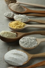 Different types of flour in spoons on light grey table, closeup