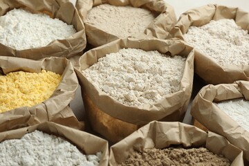 Different types of flour in paper bags on white table, closeup