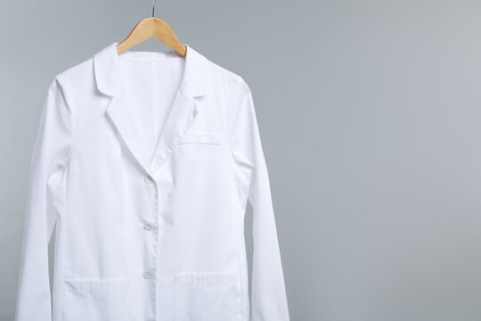 Doctor's coat on hanger against grey background. Space for text