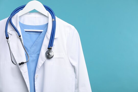 Doctor's coat with stethoscope on hanger against blue background, closeup. Space for text