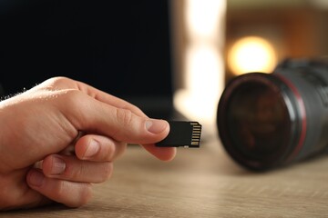 Man with SD memory card at wooden table indoors, closeup