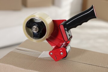 Dispenser with adhesive tape on cardboard box indoors, closeup