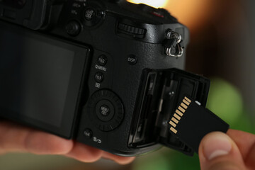 Man inserting SD memory card into photo camera indoors, closeup