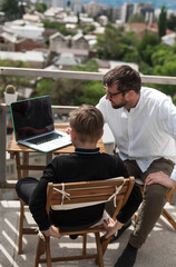 Outdoor learning with teacher and student using a laptop overlooking city rooftops. Bright sunlight, modern tutoring, remote education, digital skills in an inspiring urban setting