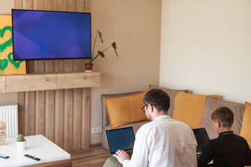 Modern digital classroom with teacher and student using laptops. Learning programming or digital skills remotely. Wall monitor, remote education, homeschool, tech-savvy environment.
