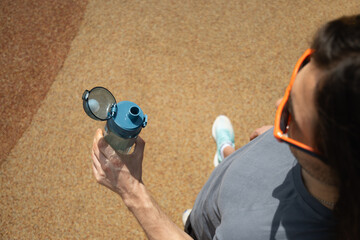 Sporty man holding water bottle in gray t-shirt on outdoor sports ground. Concept water balance for...