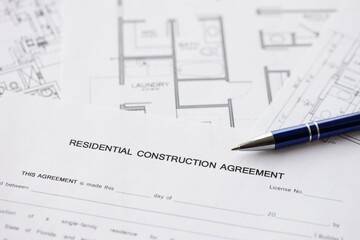 Pen on residential construction agreement and planning blueprints of residential building project