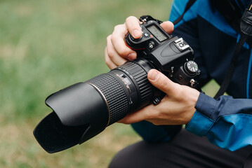 black dslr camera in hands, large long lens, young caucasian man photographer at work outdoors in sunny summer day