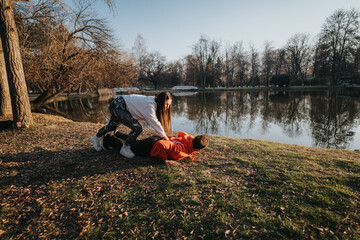 Two individuals share an active and fun outdoor moment by the serene lakeside in a park,...