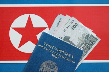 North Korean won money bills in big amount and passport lies on People Republic of Korea flag