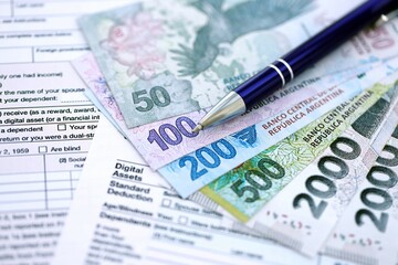 Argentine pesos money bills in big amount lies on table with pen and tax forms close up