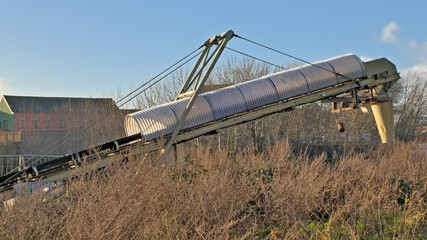 Obraz premium Detail of a conveyor belt in shrubland, industrial remains in the old docks of the port of Ghent, Belgium 