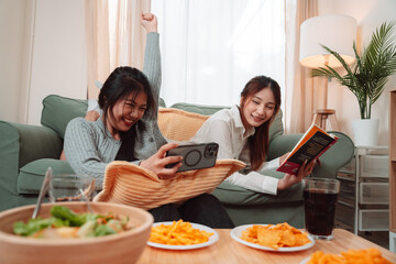 Asian Woman Friend Doing Lifestyle Indoor Smiling Phone Happiness, Sharing Joy and Memories Together at Home, Relaxing on Sofa with Smart Devices and Family Bonding Moments
